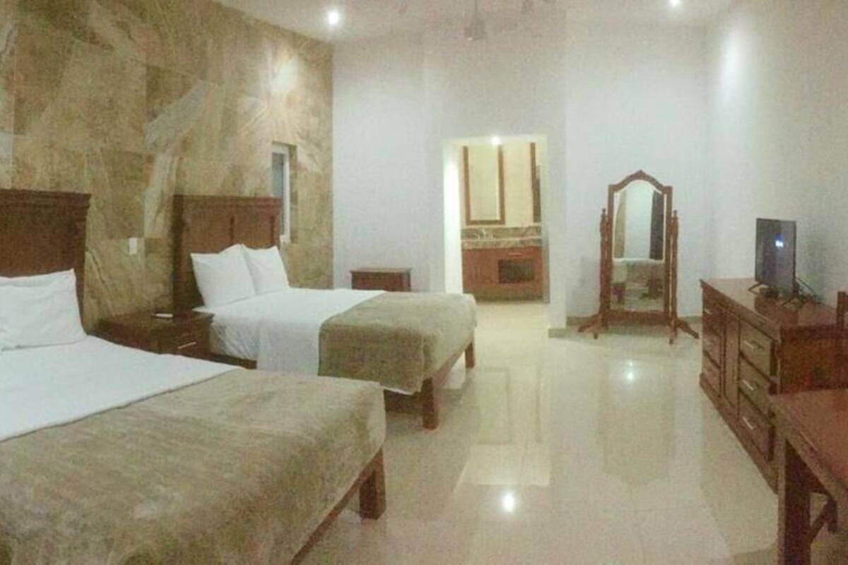 A hotel room with two beds, a wooden dresser, a mirror, and a television.