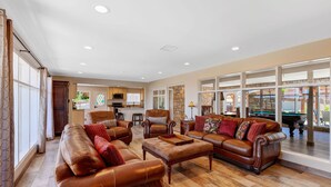 A spacious living room with leather sofas, a coffee table, and a pool table.