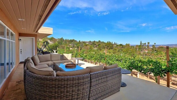 A covered outdoor seating area with a wicker sofa and a table, overlooking a vineyard.