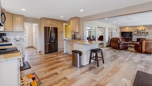 A spacious kitchen with a central island, a dining area with a stone fireplace, and a living room with leather sofas.