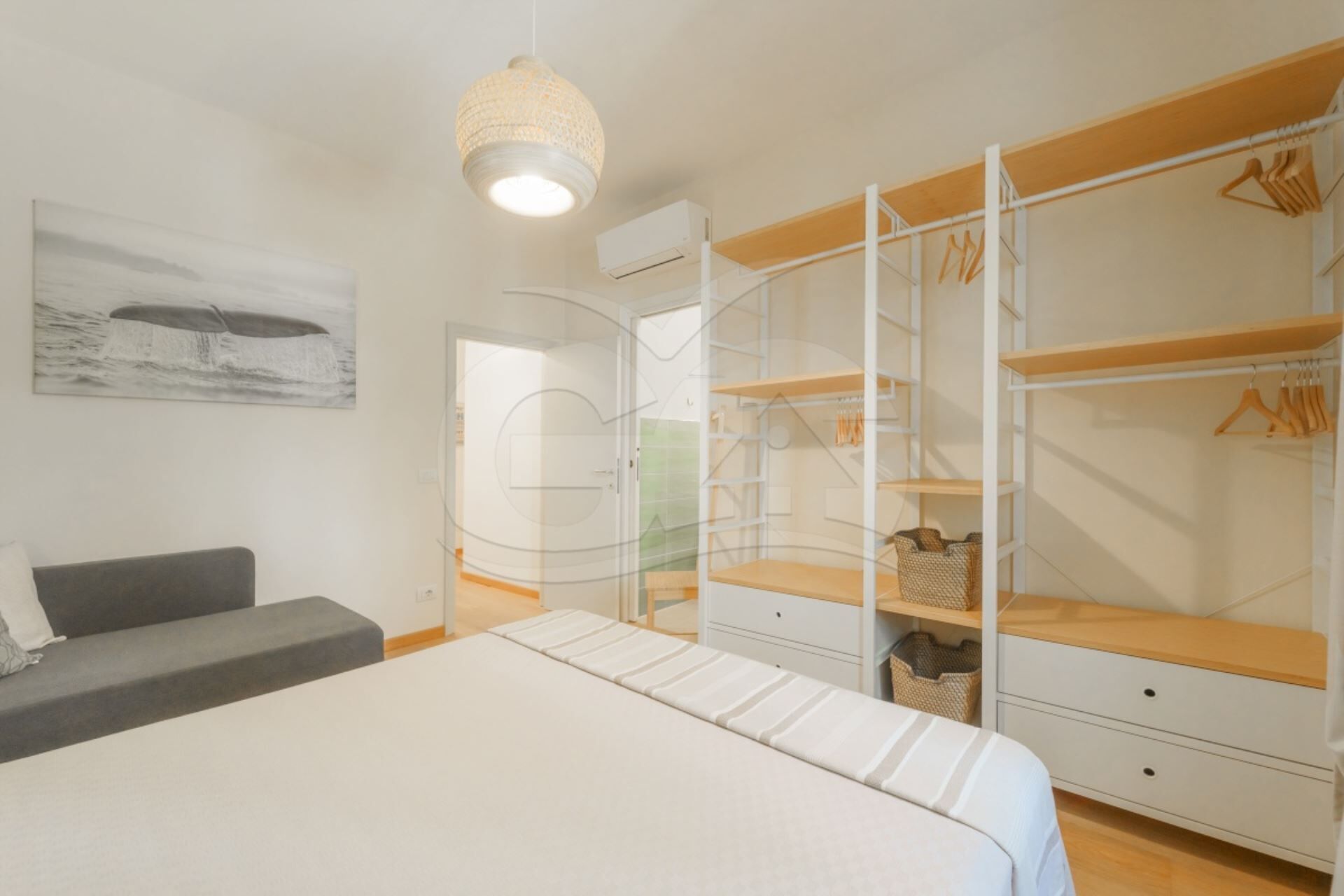 Ein Schlafzimmer mit Bett, einer Garderobe mit mehreren Regalen, einer Pendelleuchte und einem Bild an der Wand.