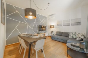 Un salon moderne avec un coin repas, agrémenté d’un motif géométrique sur le mur, d’un canapé, d’une table basse et d’un téléviseur.