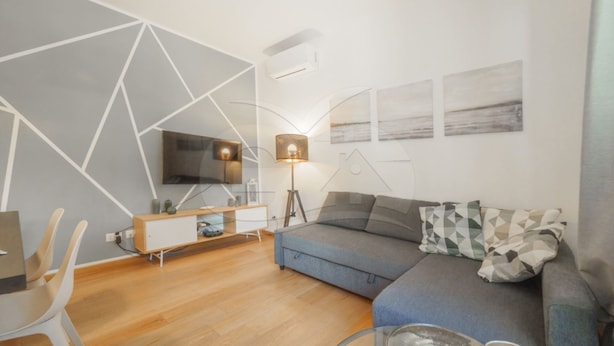 En moderne stue med en buet sofa, et fjernsyn monteret på væggen, en gulvlampe og et lille bord.