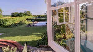 A view from a window overlooking a well-maintained garden with a swimming pool, a brick patio, and a variety of plants. - Little Pontus (Canterbury)