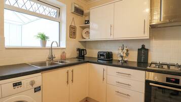 A compact kitchen with a washing machine, a toaster, a coffee maker, and a stove.