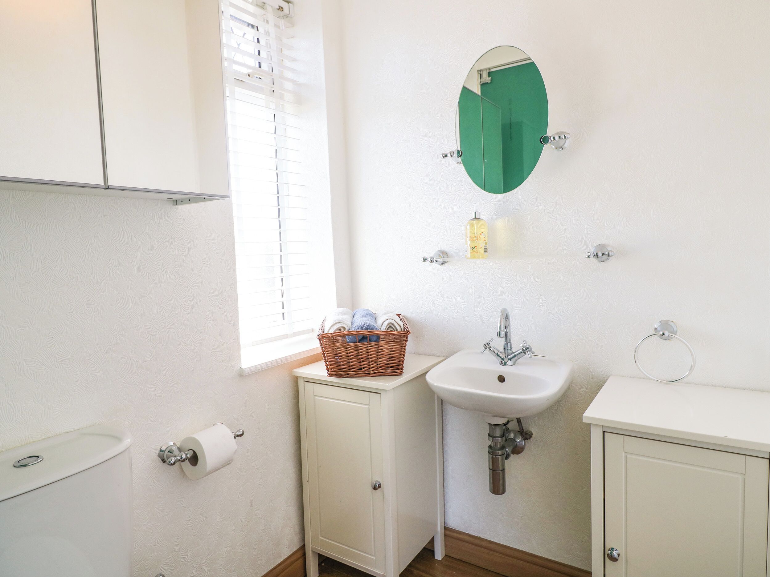 A small bathroom with a toilet, a sink, a mirror, and a window with blinds.
