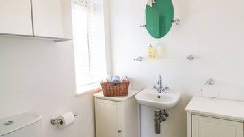 A small bathroom with a toilet, a sink, a mirror, and a window with blinds.