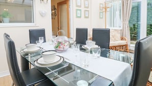 Uma área de jantar com mesa de vidro posta para seis pessoas, rodeada por cadeiras pretas.