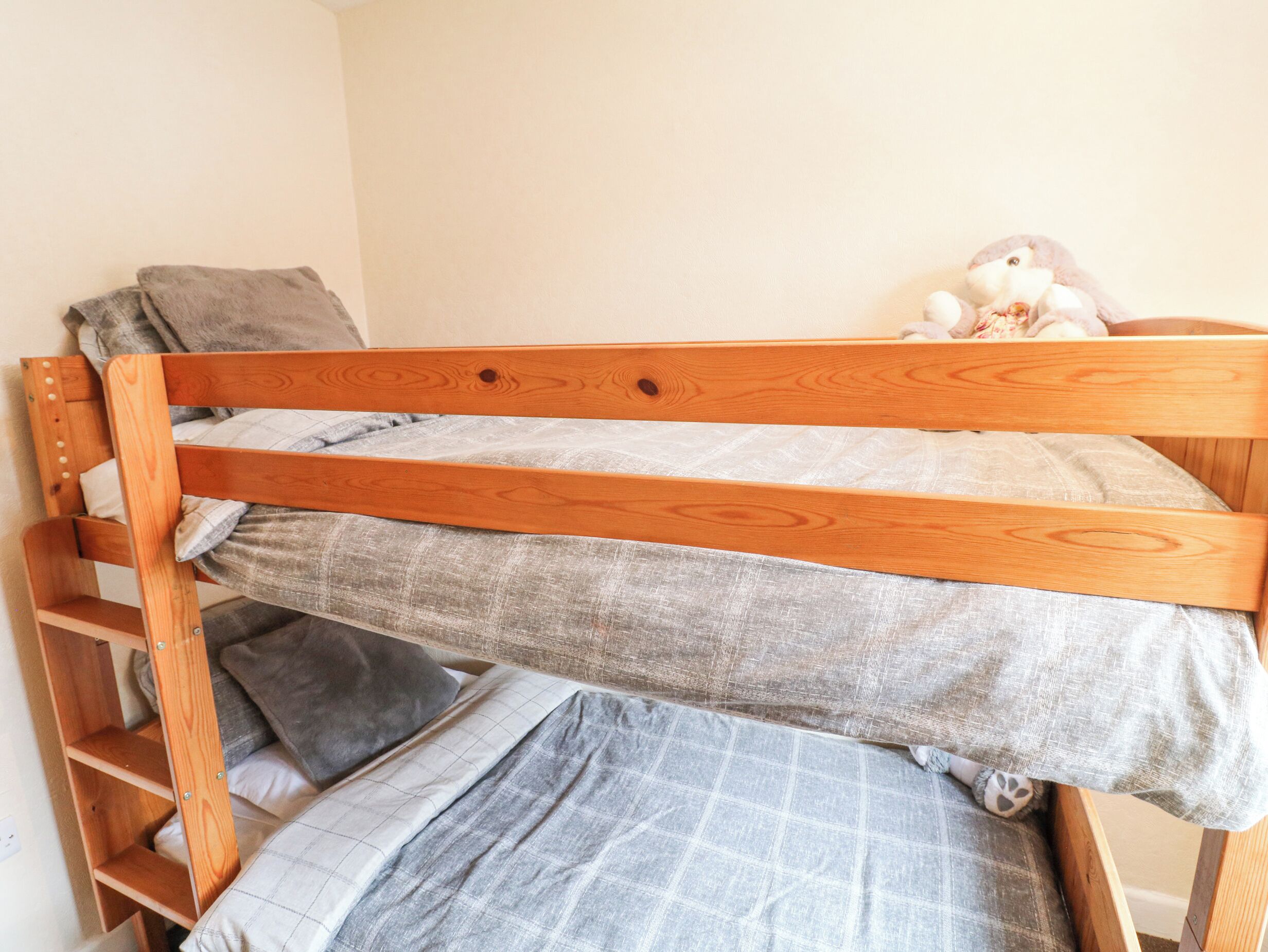 Una cama litera con estructura de madera y ropa de cama gris.