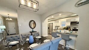 A dining area with a dark wooden table set for six, light blue upholstered chairs, and a modern chandelier.