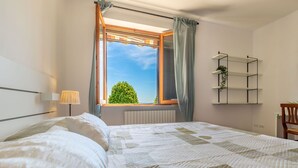 Une chambre à coucher avec un lit, une fenêtre avec des rideaux, un radiateur et une étagère sur laquelle se trouve une plante.