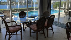 Ein Zimmer mit Glastisch und Korbsesseln, mit Blick auf einen Pool und einen Yachthafen mit Booten.