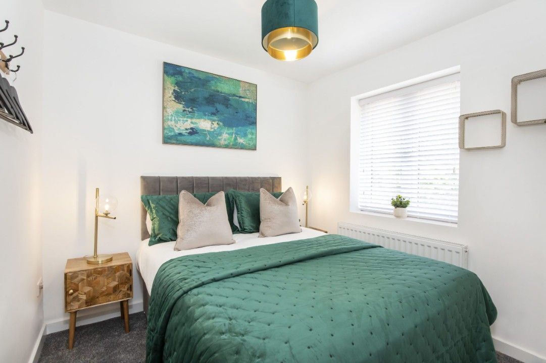 Une chambre à coucher avec un lit, une table de chevet, une lampe, une fenêtre avec des stores et un tableau au mur.