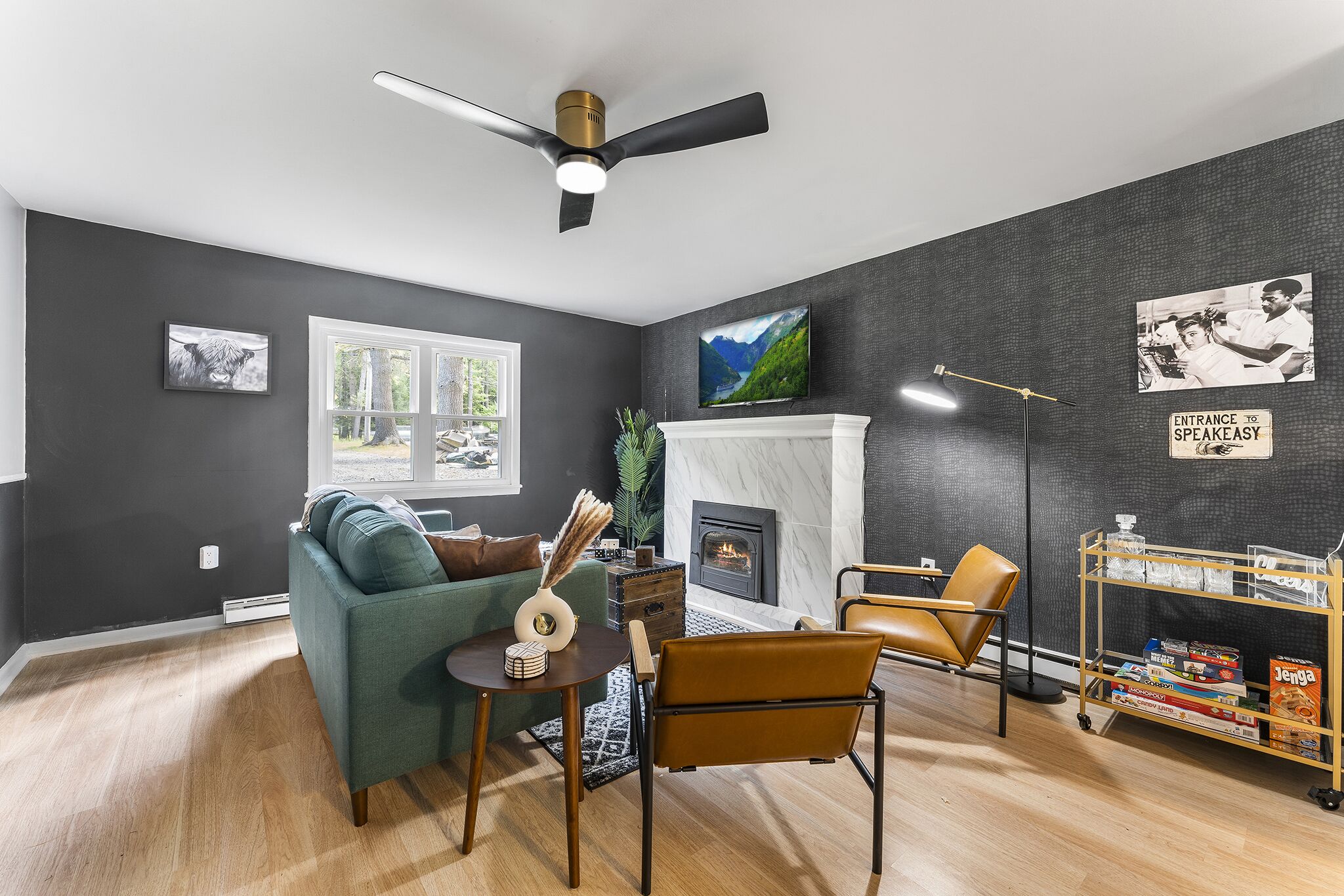 A modern living room with a fireplace, a ceiling fan, and a bookshelf.