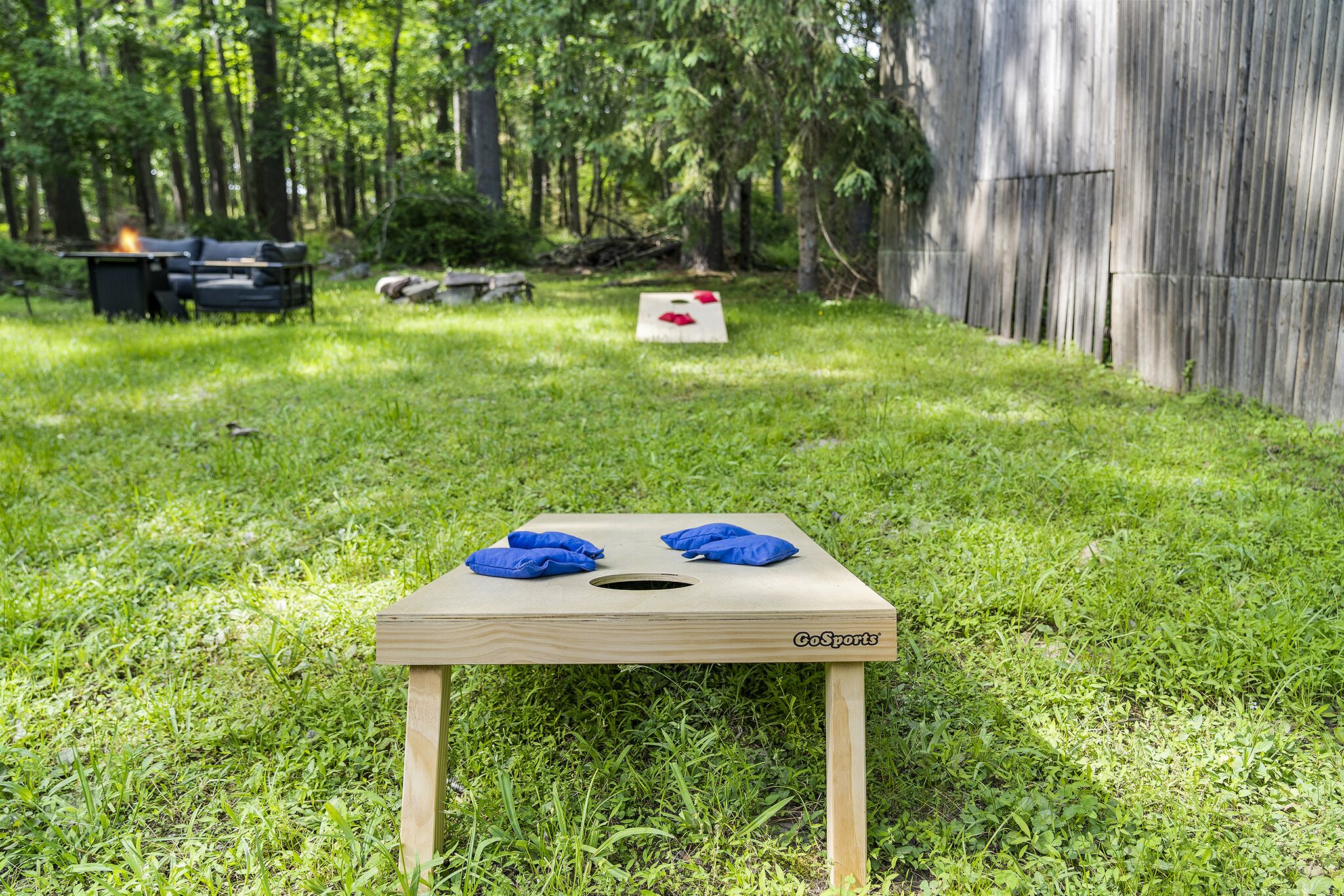 A GoSports mini disc golf basket in a grassy backyard with a wooden fence and a couch in the background.