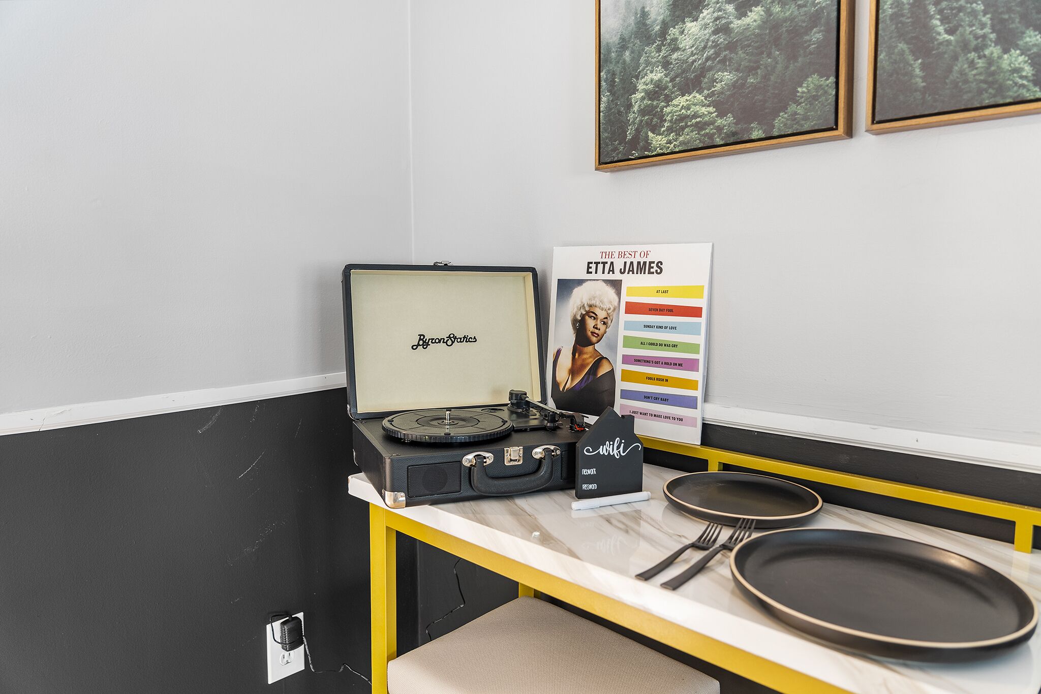 Habitació amb una taula que té un giradisc, una fotografia de dona emmarcada i un pòster d'àlbum musical.