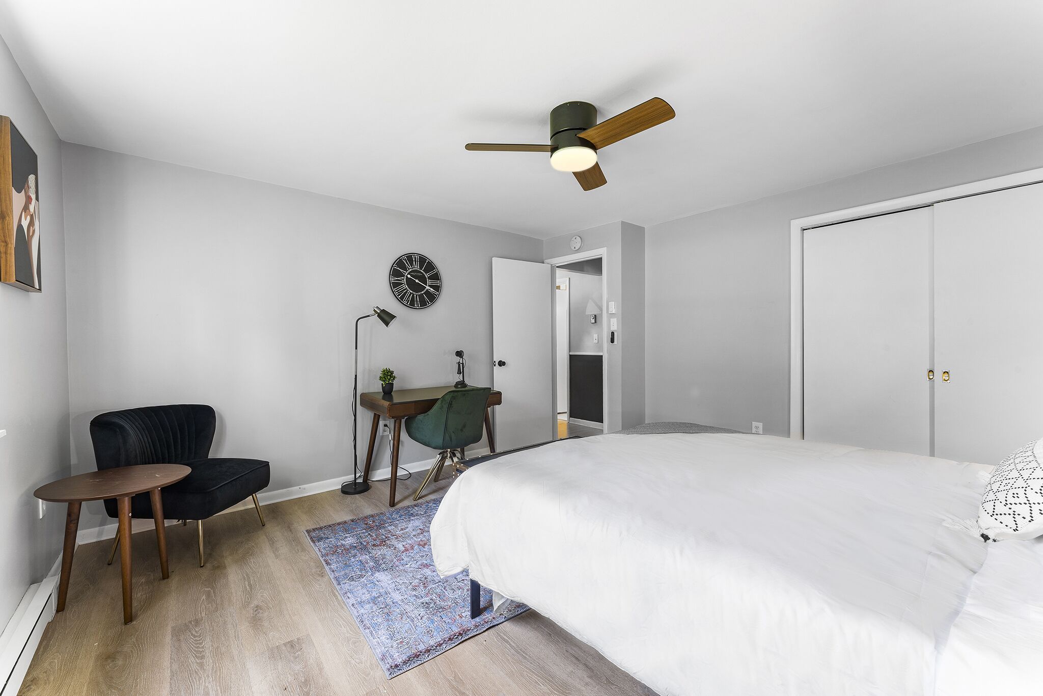 Une chambre à coucher comprenant un lit, un bureau, une chaise, un ventilateur de plafond et une porte.