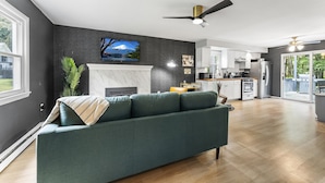 A modern living room with a green sofa, a fireplace, and a kitchen in the background. - Retro Countryside Cabin | Cozy Upstate NY Private Retreat! (Eldred)
