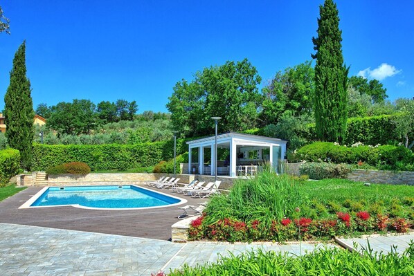 A pool area with lounge chairs, a gazebo, and a landscaped garden with various plants and flowers.