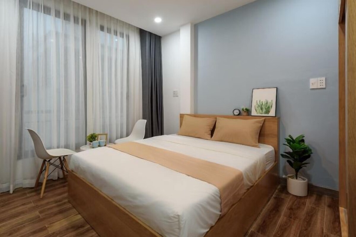 A bedroom with a bed, a chair, a small table, and a potted plant.