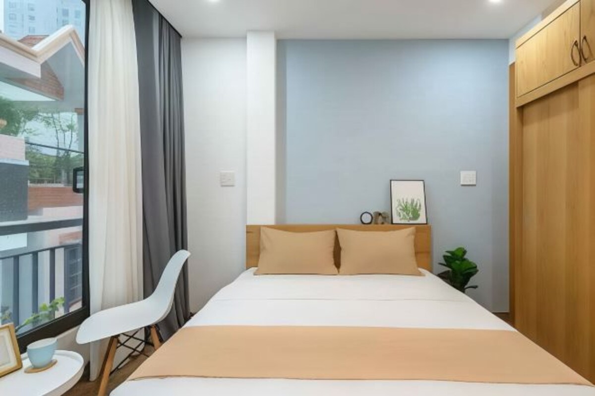 Habitación de hotel ordenada con cama, una silla, una mesita y una ventana con cortinas.