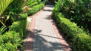 A paved pathway leading to a building with a thatched roof, surrounded by lush greenery and tall trees. - Bungalows Punta Uva (Cahuita)