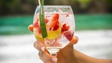 A hand holding a clear glass with a drink garnished with fruit and a straw.