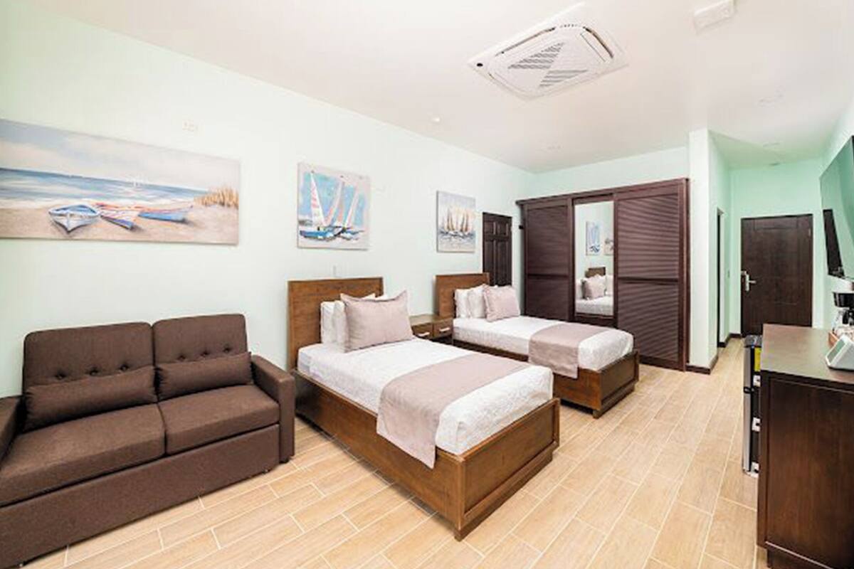 A hotel room with two beds, a sofa, a desk, and artwork on the walls.