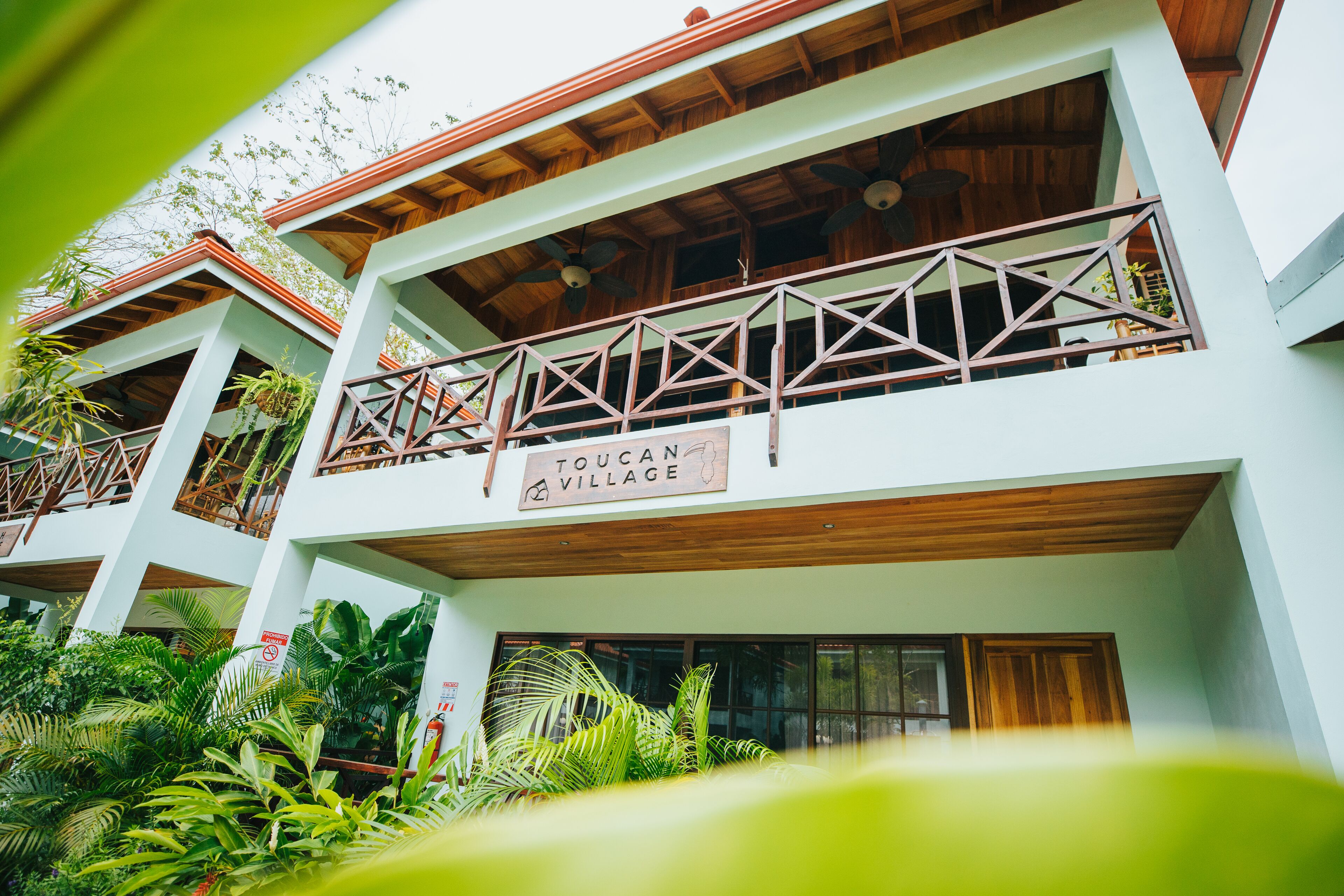 A multi-story building with balconies, wooden beams, and a sign reading "TOUCAN VILLAGE".
