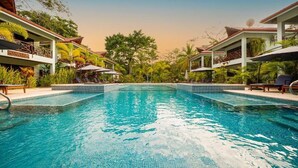 A swimming pool with lounge chairs and umbrellas, surrounded by greenery and buildings. - Bungalows Punta Uva (Cahuita)