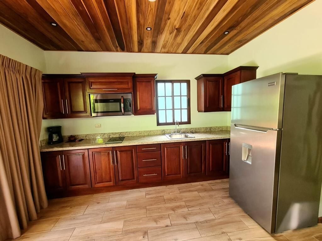 A kitchen with wooden cabinets, a stainless steel refrigerator, and a herringbone-patterned floor.