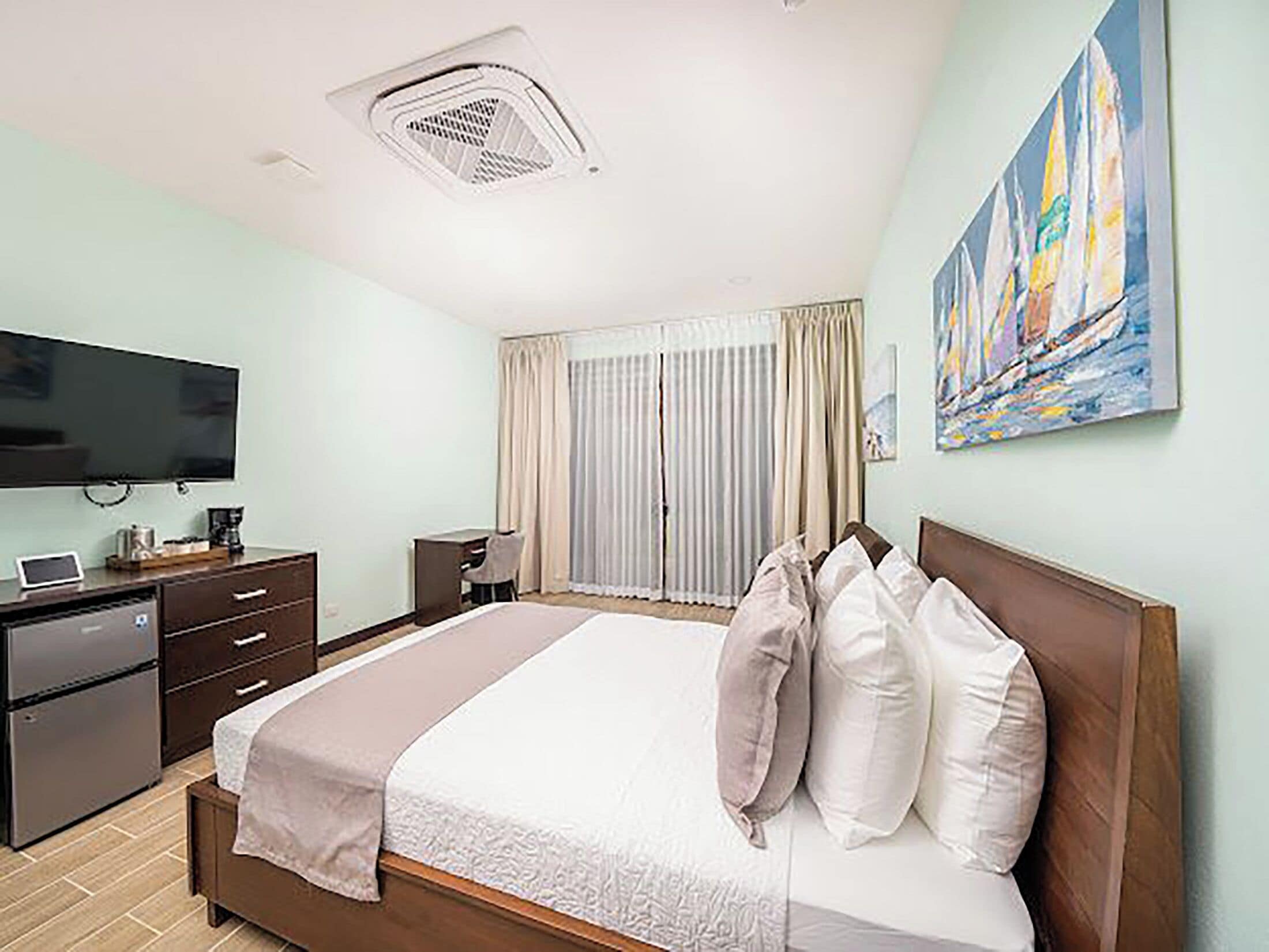 A hotel room with a bed, a desk, a television, and a painting on the wall.