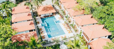 Vista aérea de un resort con varias cabañas y una piscina central, rodeado de palmeras.