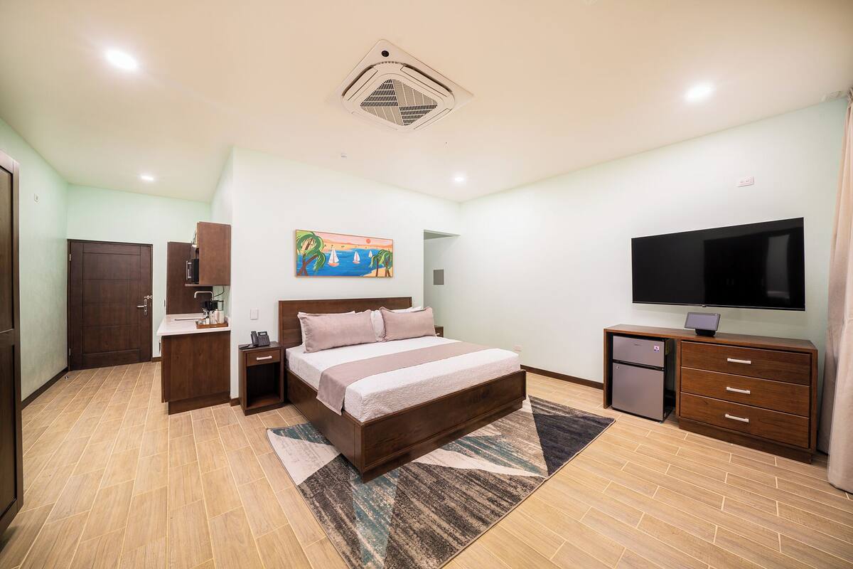A bedroom with a bed, bedside tables, a TV, a small refrigerator, and a painting on the wall.