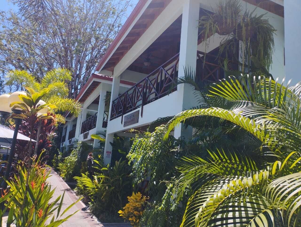 A building with a covered walkway, surrounded by lush tropical plants.