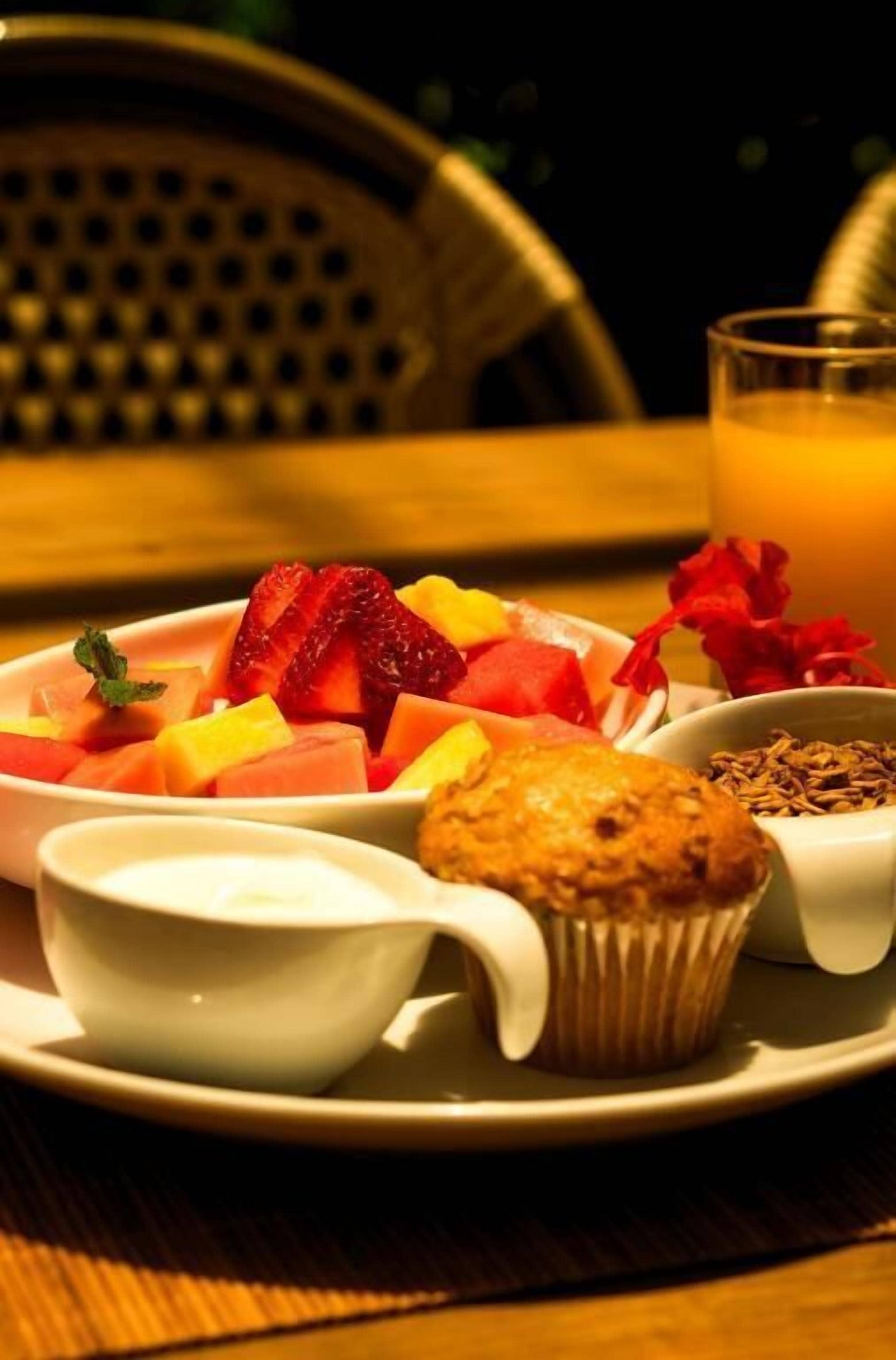 Een ontbijt bord met fruit, een muffin en een glas sinaasappelsap op een tafel.