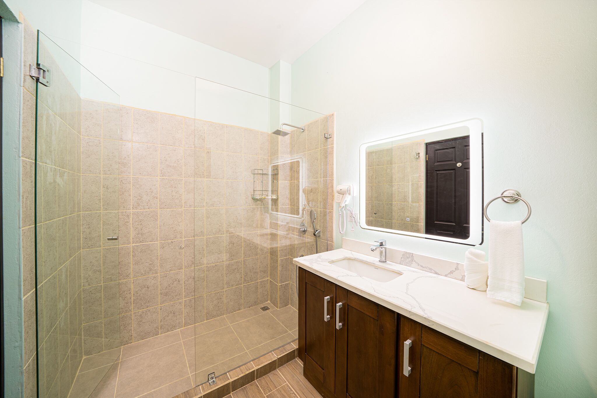 Un bany modern amb dutxa envidrada, un lavabo de marbre i armaris de fusta.