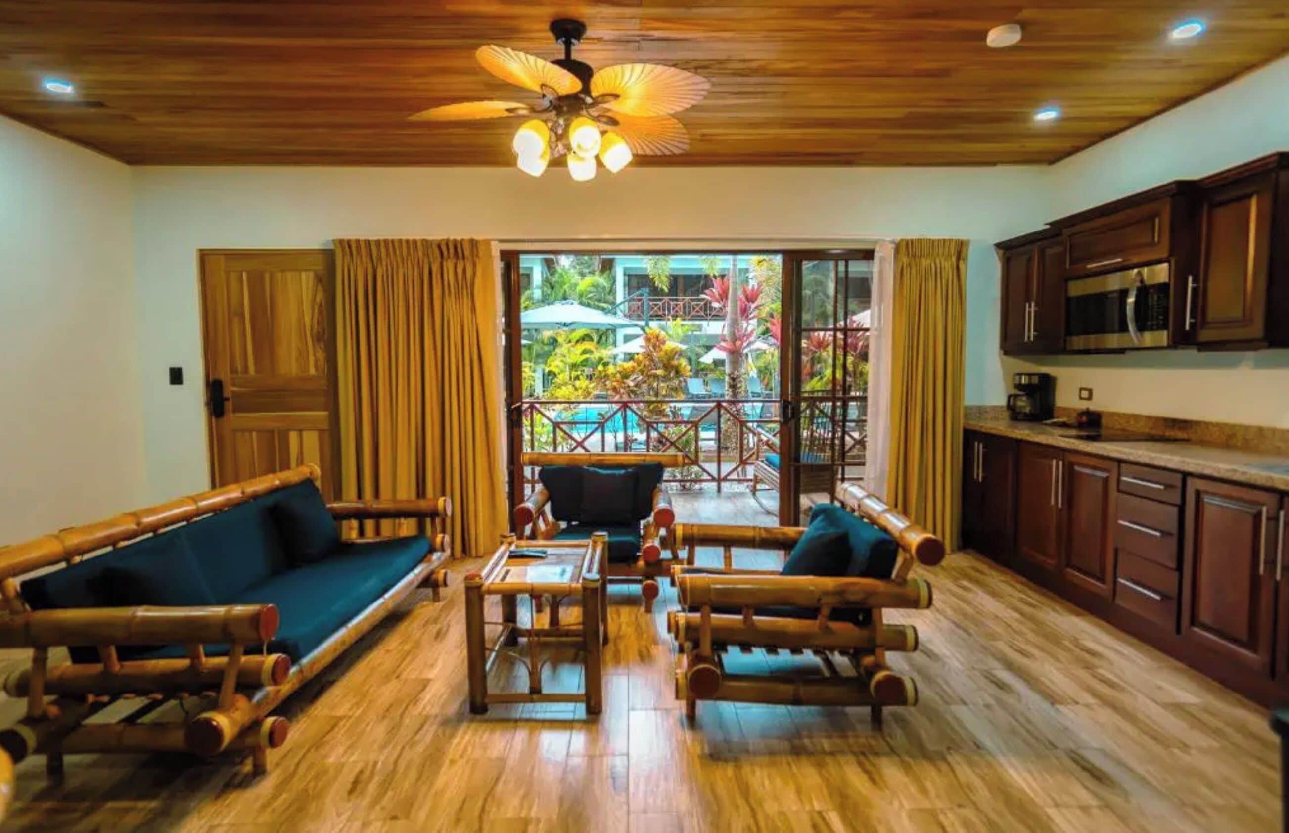 Una habitación con techo de madera, ventilador de techo, sofá, mesa de centro y una zona de cocina con armarios y microondas.