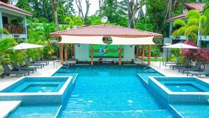 A pool area with a covered seating area, lounge chairs, and a view of a tennis court.