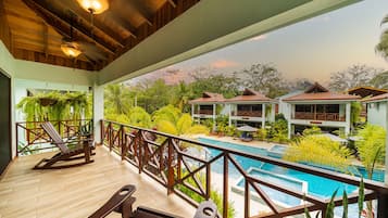 Relax on the balcony with a view of the pool surrounded by lush greenery.
