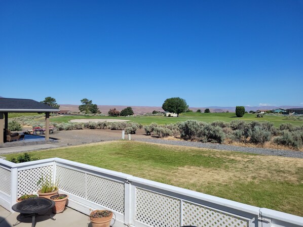 A patio with outdoor furniture and potted plants, overlooking a well-maintained lawn and distant hills. - 6th Hole Loop in Desert Aire (Mattawa)