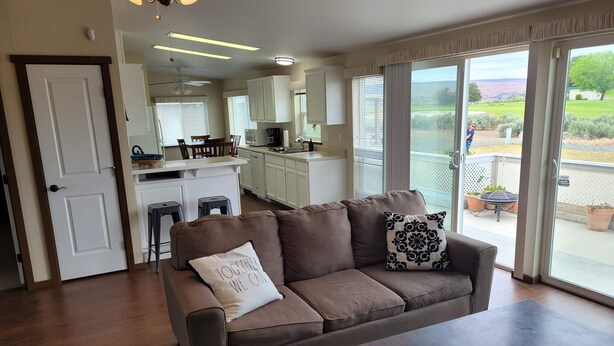 Een woonkamer met een bruine bank, een bijzettafeltje, en uitzicht op een keuken en terras.
