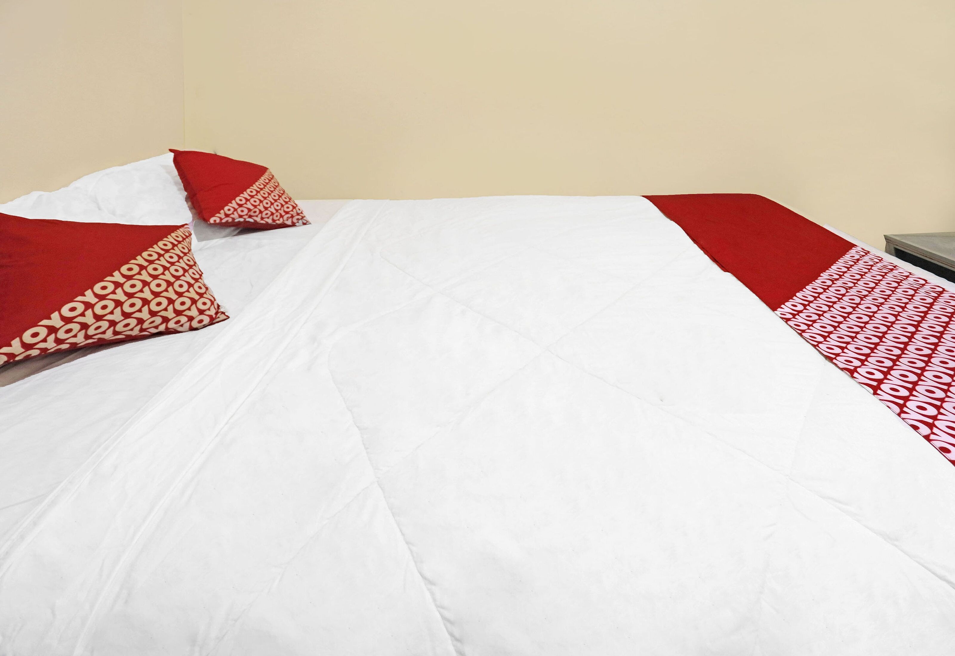 Een bed met witte lakens en rode kussens met een patroon.