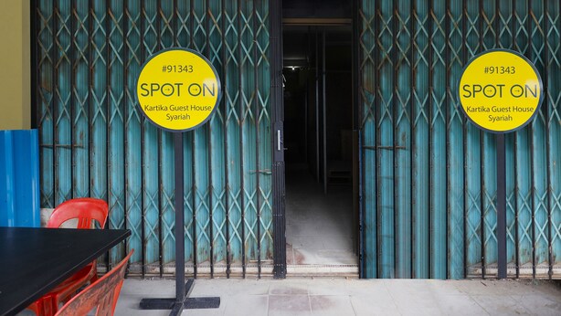 Een gebouw-ingang met twee gele borden waarop 'SPOT ON' en 'Kartika Guest House Syariah' staat, met een nummer '#91343'.