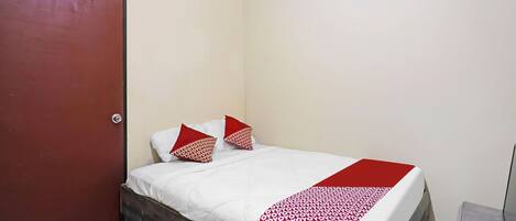 A single bed with a wooden frame, white bedding, and two red pillows with a pattern.