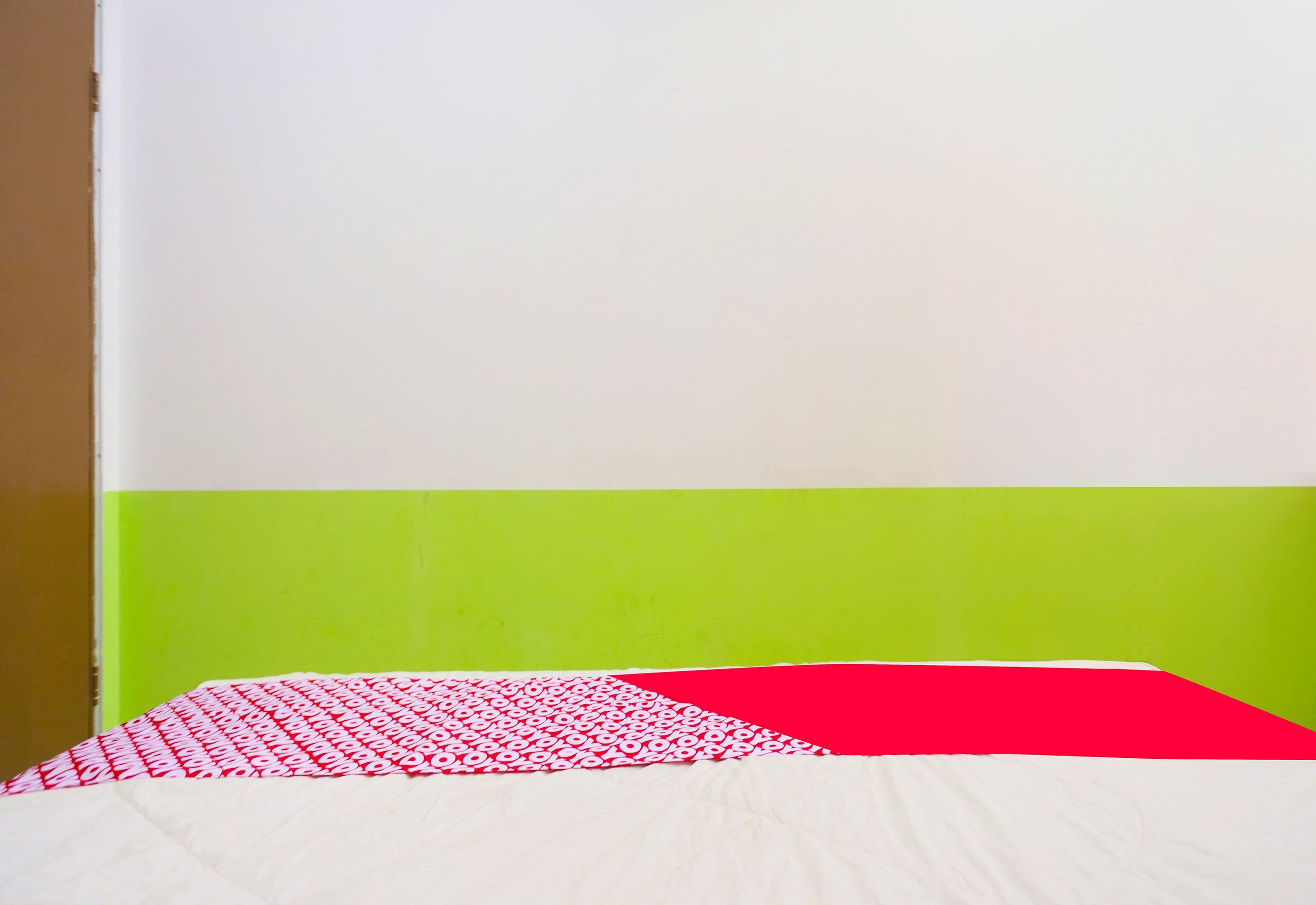 A bed with a white and red patterned bedspread, a green wall, and a white ceiling.