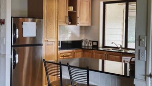 Une cuisine moderne avec des meubles en bois, un réfrigérateur en acier inoxydable, un plan de travail noir et une fenêtre équipée de stores.