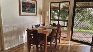 Un coin repas avec une table et des chaises en bois, un tableau encadré au mur et une vue à travers une porte vitrée.