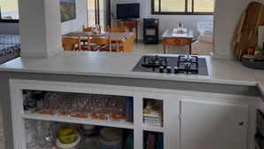 A modern kitchen with a gas stove, a dining area with a table and chairs, a TV, and a view of the beach.