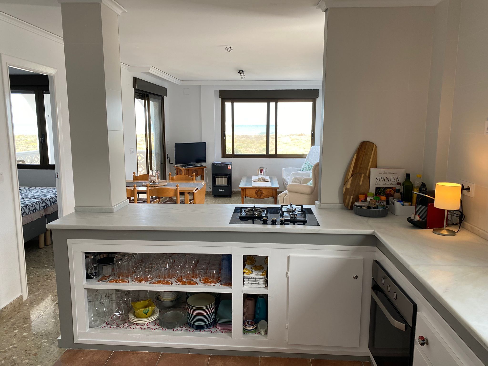 Une cuisine compacte avec un four encastré, un coin repas avec une table et des chaises, un téléviseur et une vue sur la plage.